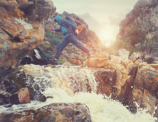 man crossing river in mountains with backpack