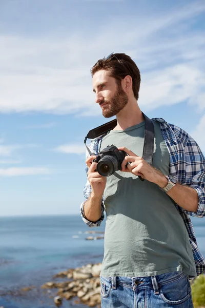 Unga, attraktiva man står nära havet med digital camer — Stockfoto