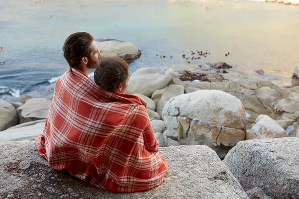 Pareja acurrucada sentada en las rocas, con vistas al océano — Foto de Stock