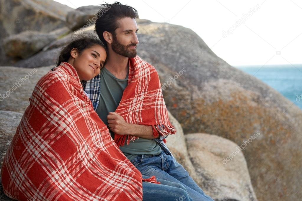 Cuddled couple sitting on the rocks, overlooking the ocean