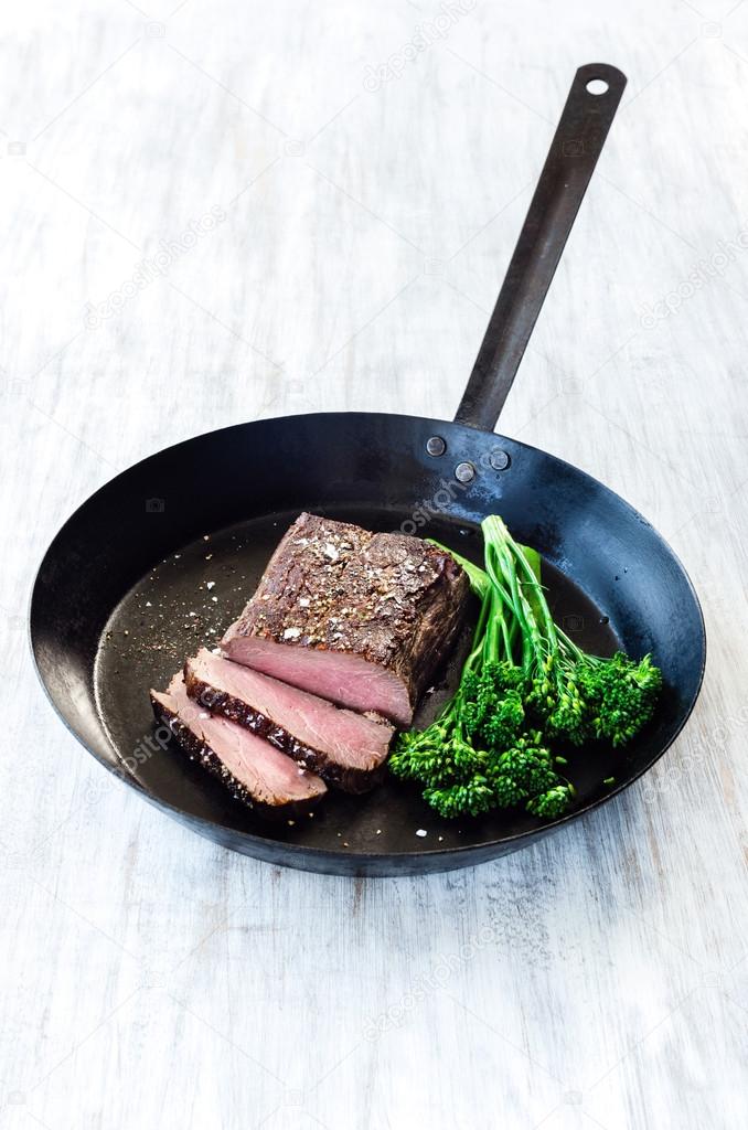 Juicy steak on black pan with fresh green vegetables 