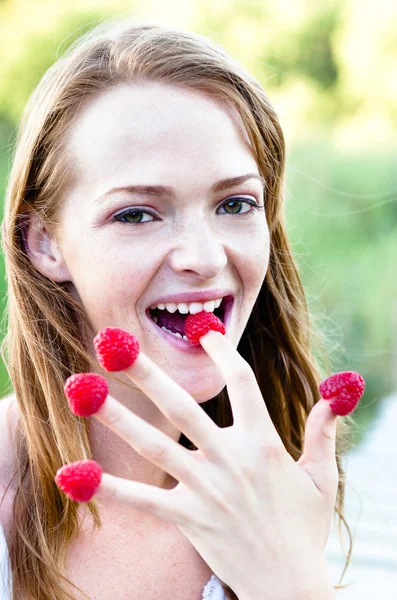 Woman eating raspberries off her fingers outdoors — Stok fotoğraf