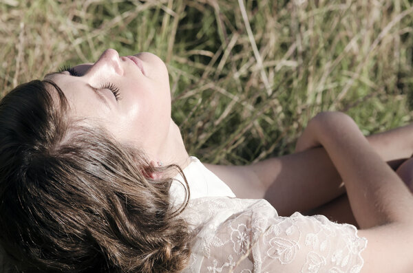 Beautiful young lady in lace sits in long grass and enjoys the sunshine on her face