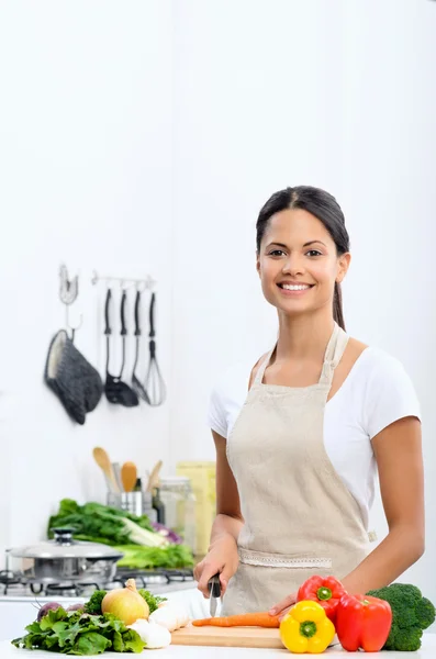 Mulher sorridente cortando legumes em uma cozinha — Fotografia de Stock