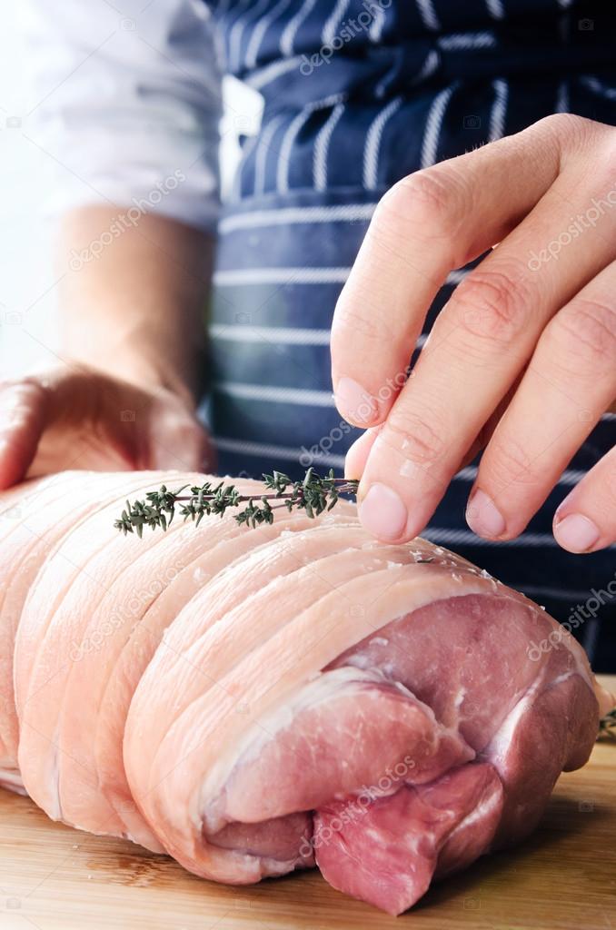 Chef hands seasoning raw pork shoulder with fresh thyme