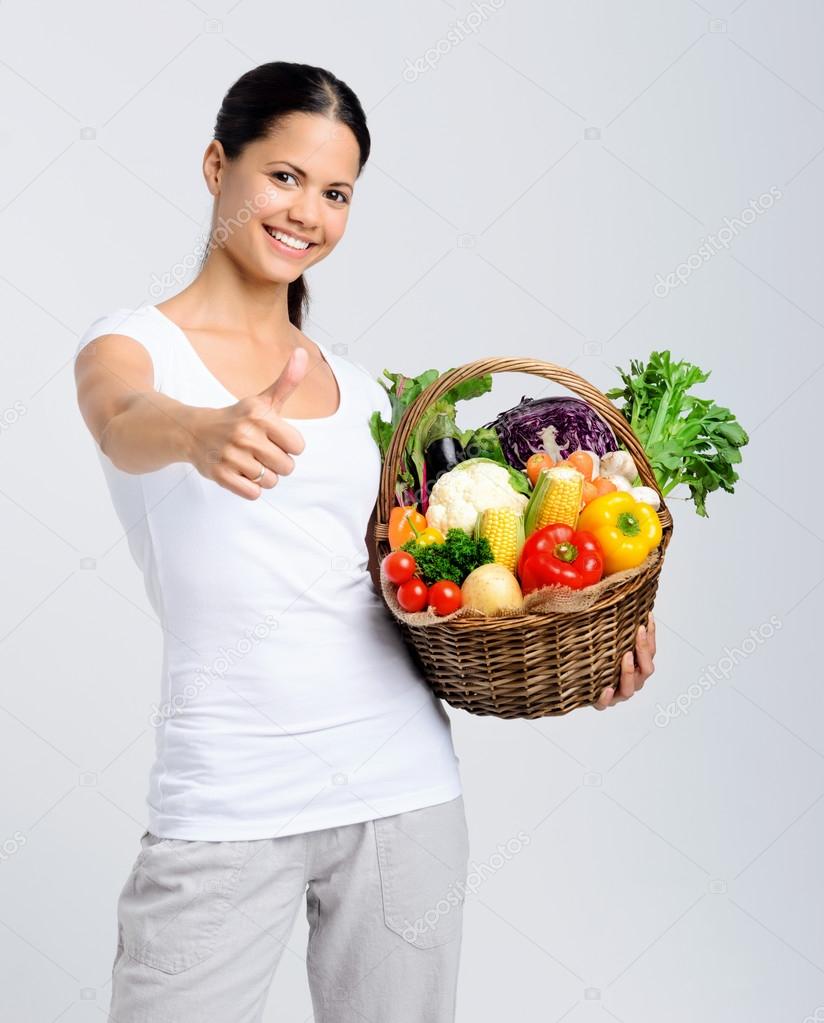 Happy woman holding basket of raw vegetables