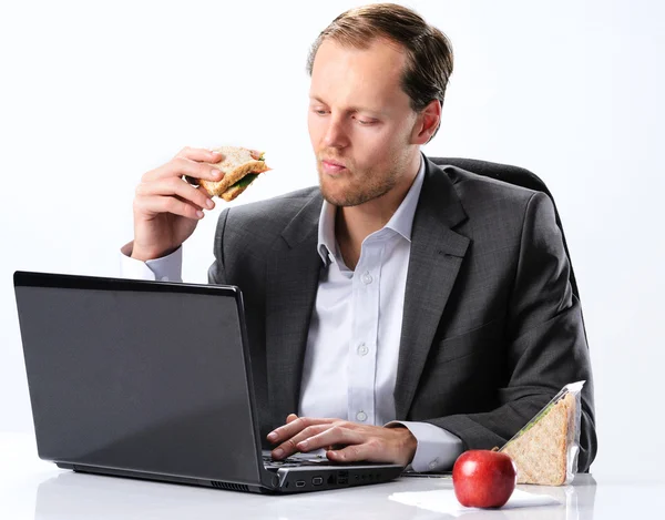 Un homme travailleur mange à son bureau — Photo