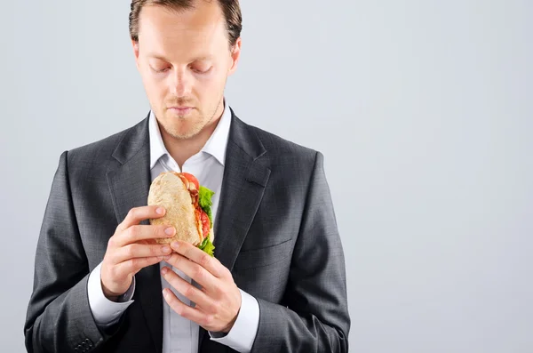 Man in business suit eating a delicious take away meat roll — Stock Photo, Image