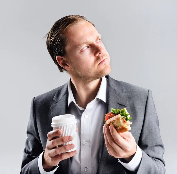 Busy businessman eating takeaway sandwich — Stockfoto
