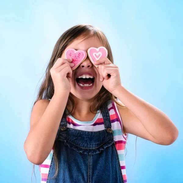 Niña sostiene galletas en forma de corazón sobre sus ojos —  Fotos de Stock