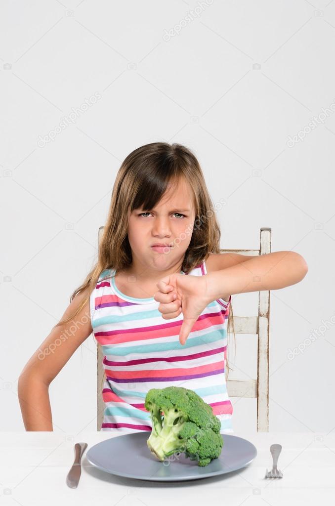 Cute young child kid making disgusted disapproving face at her food, healthy eating food choice concept