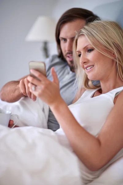 Par med mobil mobiltelefon avkopplande i sängen — Stockfoto