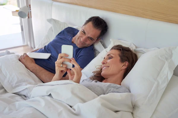 Casal usando tablet digital e telefone celular na cama — Fotografia de Stock