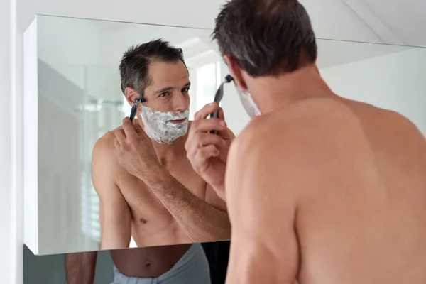 在镜子用剃刀刮胡子的男人 — 图库照片