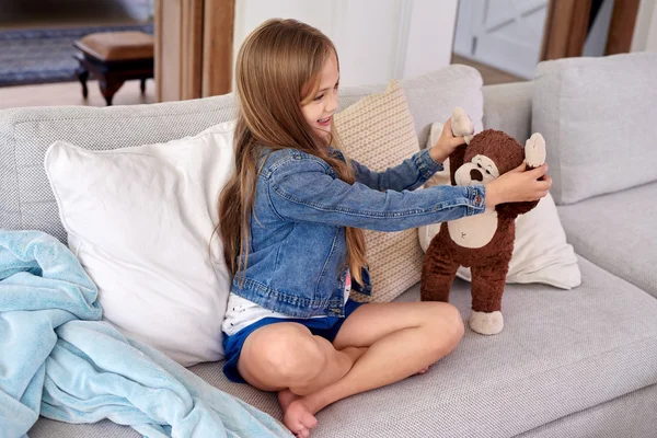 Chica jugando con marrón osito de peluche en sofá —  Fotos de Stock