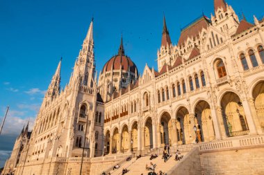 Budapeşte, Macaristan - 29 Eylül 2024: İnsanlar Budapeşte, Macaristan 'daki kuleleri ve kubbesiyle Meclis binasının önündeki basamaklarda