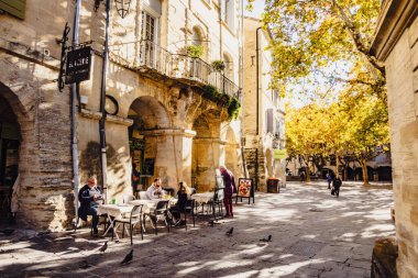 Uzes, Fransa - 20 Kasım 2023: Evler ve İnsanlar Uzes kasabasının merkezindeki bir sokakta terasta oturuyorlar