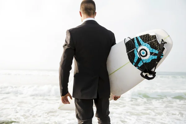 Бизнесмен держит свою доску для серфинга на песчаном пляже — стоковое фото