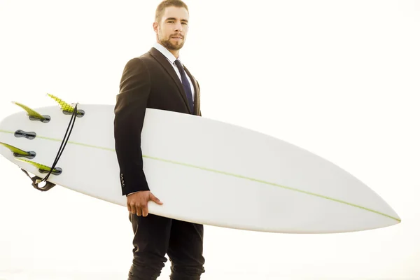 Affärsman håller sin surfbräda på sandstrand — Stockfoto