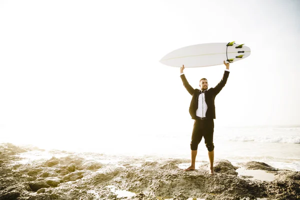 Empresario sosteniendo su tabla de surf en la playa de arena —  Fotos de Stock