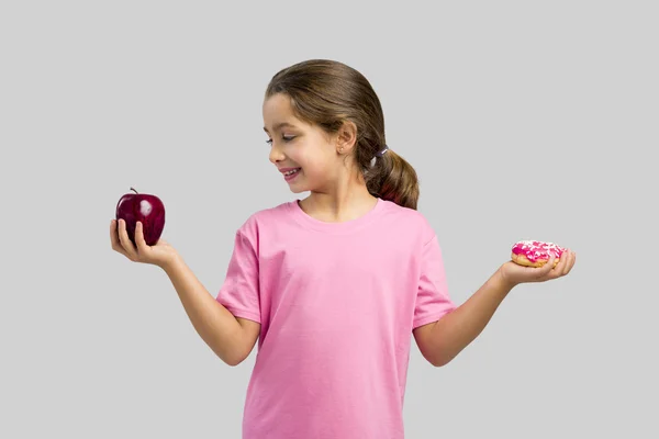 Menina escolhendo entre uma maçã e um donut — Fotografia de Stock