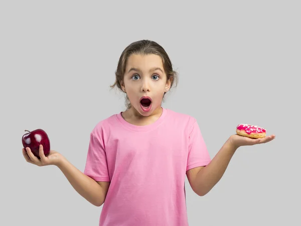 Menina escolhendo entre uma maçã e um donut — Fotografia de Stock