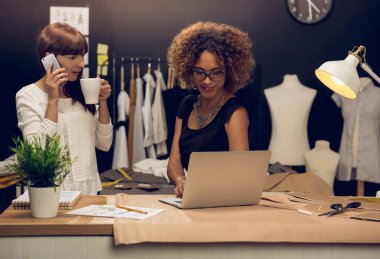 İki genç girişimci kadın ve moda tasarımcısı atölyesinde çalışıyor.