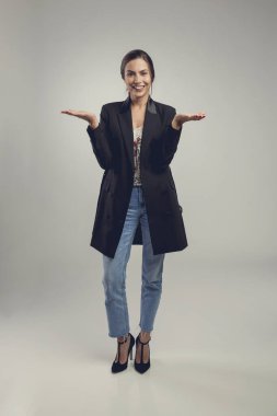 Gri arka planda güzel ve kendinden emin genç bir kadın ellerini gösteriyor.