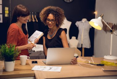 İki genç girişimci kadın ve atölyede çalışan moda tasarımcıları.