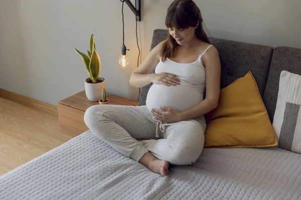 幸せな妊娠中の女性座っていますベッドとタッチ彼女の腹に家 — ストック写真