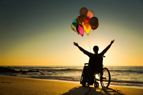 ビーチでカラフルな風船を持つ車椅子の上の障害者 — ストック写真