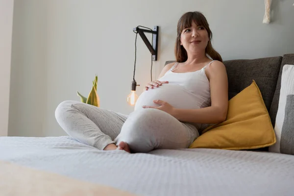 Lycklig Gravid Kvinna Sitter Sängen Och Rör Vid Magen Hemma — Stockfoto