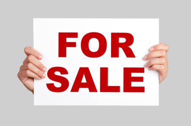 Satılık ilan panosu tutan kadın eller.