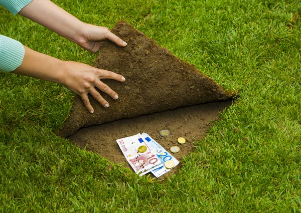 Hände verstecken Geld unter dem Gras — Stockfoto