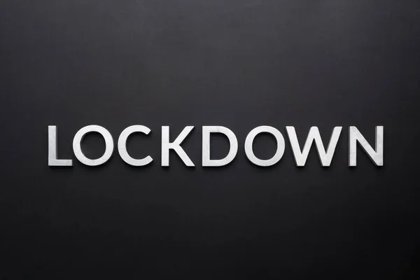 「ロックダウン」という言葉は真上の真っ黒の背景にシルバーメタルの文字で書かれています — ストック写真
