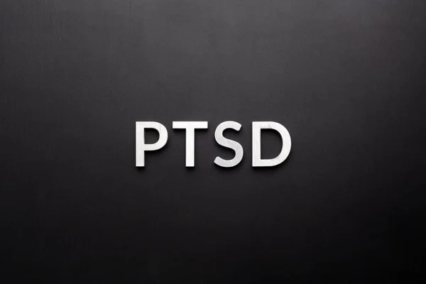 Słowo PTSD ułożone srebrnymi metalowymi literami na płaskim czarnym tle bezpośrednio nad perspektywą — Zdjęcie stockowe