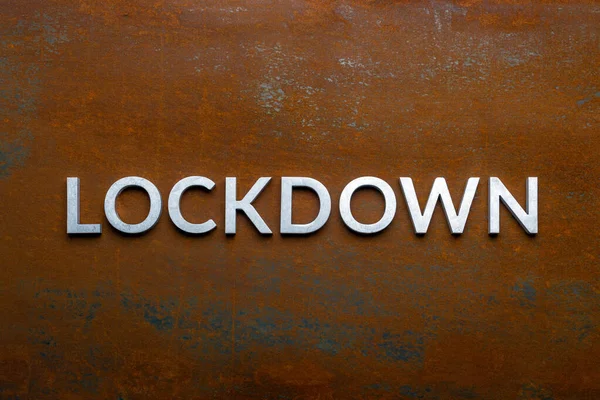 Слово lockdown, написанное серебряными металлическими буквами на плоском ржавом стальном фоне прямо над горизонтом — стоковое фото