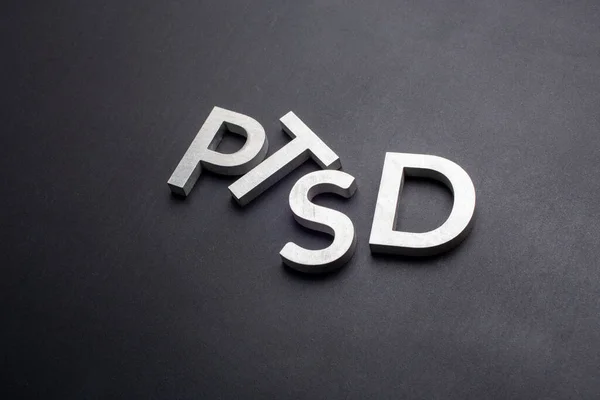 the word PTSD - post traumatic stress disorder - laid with silver metal letters on flat black background in slanted linear perspective