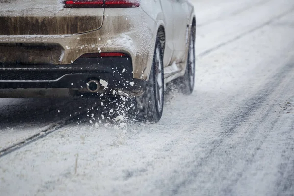 Pezzi di neve stradale scorrono da ruote di sporca auto bianca che si muovono velocemente nella città luce del giorno con attenzione selettiva. — Foto Stock