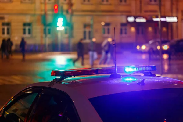 Night police car lights in city street with blurry pedestrians crossing road in the background — Stock Photo, Image