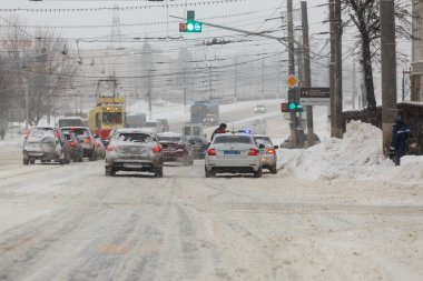 Tula, Rusya - 13 Şubat 2020: Şehir arabaları yoğun kar yağışı sırasında trafik ışıklarının önünde polis aracıyla durdu.