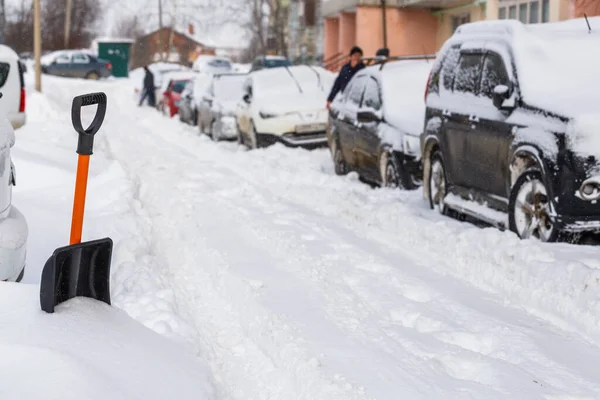 Pequeña pala de nieve de plástico cerca de los coches cubiertos de nieve en la soleada mañana de invierno — Foto de Stock