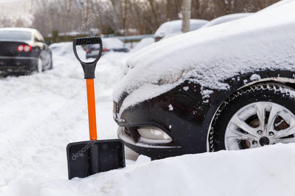 plastic snow shovel in front of snow-covered car at sunny winter morning