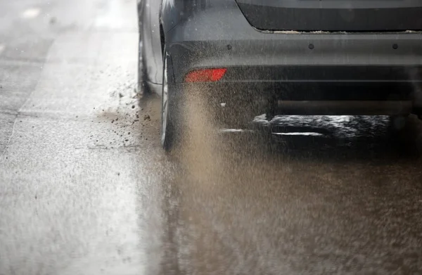 Vuil water spatten stroom van wielen van zilveren auto snel in daglicht stad met selectieve focus. — Stockfoto