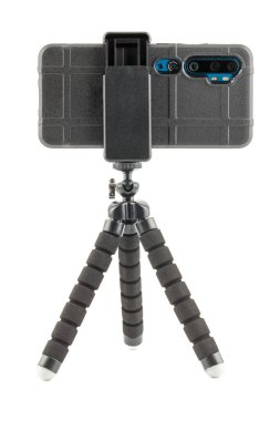 Beyaz üzerinde izole edilmiş küçük esnek tripodun üzerinde kabuklu kauçuk koruyucu kapaklı siyah cep telefonu.