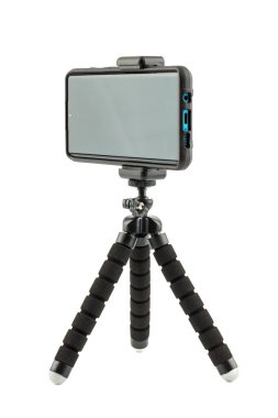 Beyaz üzerinde izole edilmiş küçük esnek tripodun üzerinde kabuklu kauçuk koruyucu kapaklı siyah cep telefonu.