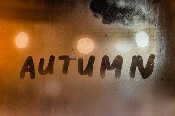 A palavra outono escrito à mão na superfície de vidro da janela molhada noite — Fotografia de Stock
