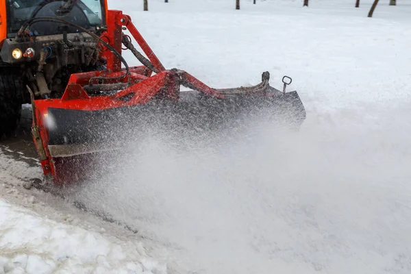 Snow cleaning. Snow removal tractor clearing snow from pavement with special round spinning brush,