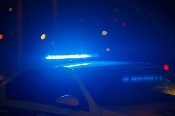 Blåt politibillys om natten i byen med selektivt fokus og bokeh på sort baggrund - Stock-foto