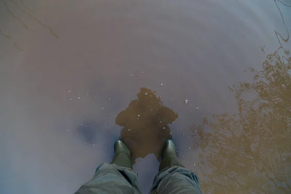Kirli kahverengi su birikintisinde duran yeşil lastik çizmeli ve yeşil pantolonlu bacaklar. — Stok fotoğraf